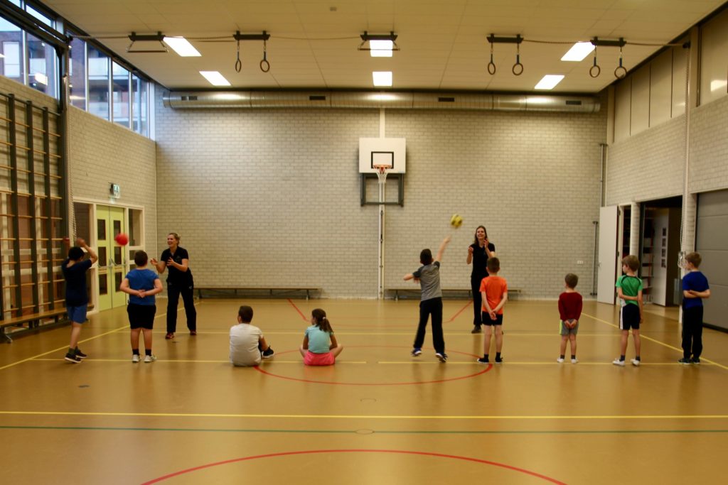 Kinderen op een rij vangen een bal tijdens groepsles